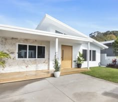 a white house with a wooden front door and two plants on the side of it