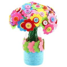 a vase filled with lots of different colored buttons on top of a white table next to a plant