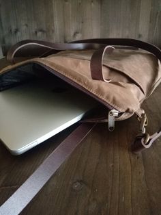 an open laptop computer sitting on top of a wooden table next to a purse and wrist strap