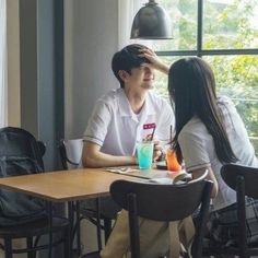 a man and woman sitting at a table in front of a window with drinks on it