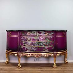 a purple and gold dresser with flowers painted on the front, sitting against a white wall