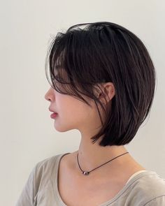 a woman with short black hair wearing a necklace and looking off to the side in profile