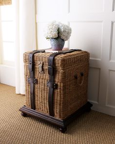 a wicker suitcase sitting on the floor next to a vase with flowers in it