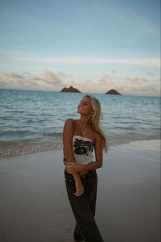 a woman standing on top of a sandy beach next to the ocean with an island in the background