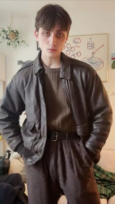 a man standing in front of a couch wearing a leather jacket and pants with his hands on his hips