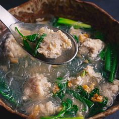 a ladle full of soup with meat and green vegetables on the side, being held by a metal spoon