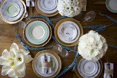 the table is set with white flowers and gold china plates, napkins, and silverware