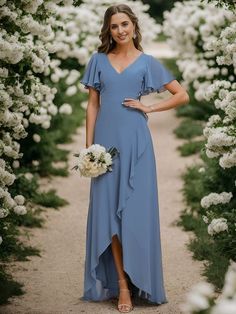 a woman in a blue dress standing under an archway with white flowers and greenery