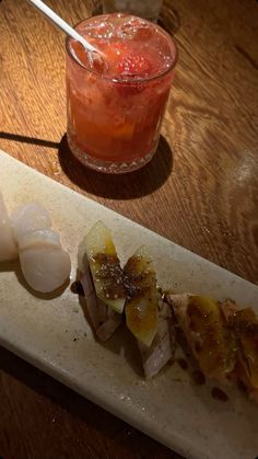 a wooden table topped with a cutting board covered in food next to a glass filled with liquid