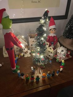 two elfs are standing next to a christmas tree and other toys on a table