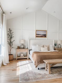 a bedroom with white walls and wood flooring has a large bed, two nightstands, and a plant in the corner