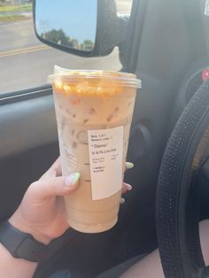 a woman holding up a cup of coffee in her car