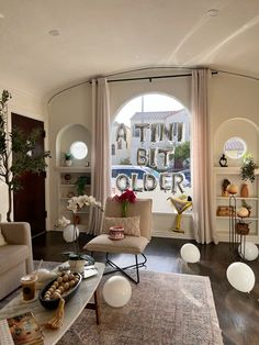 a living room filled with furniture next to a large window covered in white curtains and flowers