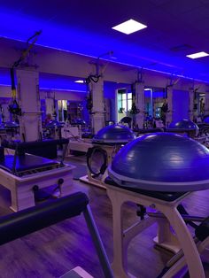 there are many exercise equipment in the gym with blue lights on them and people walking around