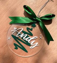 a glass ornament with green ribbon hanging on a wooden table