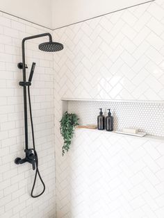 a bathroom with white tiled walls and flooring, shower head, and hand held faucet