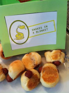 small hot dogs wrapped in buns on a plate next to a sign that says snakes in a blanket