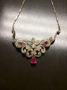 DeKara Designs A Beautiful Timeless 14K White Gold Art Deco Inspired Ruby Diamond Necklace. Metal- 14K White Gold, .583. Stones- 1 Pear Shape Pinkish Red Ruby 0.90 Carats, 2 Round Rubies 0.27 Carats, 44 Round Antique Diamonds G-H Color VS2-SI1 Clarity 1.10 Carats. Handmade Diamond Art Deco Influcned Ruby Diamond Necklace. I have used authentic antique Old European Cut and Miner's Cut diamonds for this necklace. The necklace features a beautiful pear shape ruby that is dangling on the bottom of t Diamond Ruby Necklace, Ruby Diamond Necklace, Necklace Art Deco, Pinkish Red, Art Deco Necklace, Gold Art Deco, Ruby Necklace, Antique Diamond, Ruby Diamond