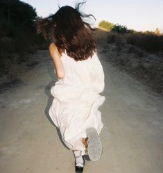 a woman walking down a dirt road with her hair blowing in the wind