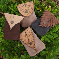 four leather purses with leaves on them sitting in the grass next to some bushes