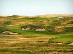 a golf course surrounded by green grass and sand dunes