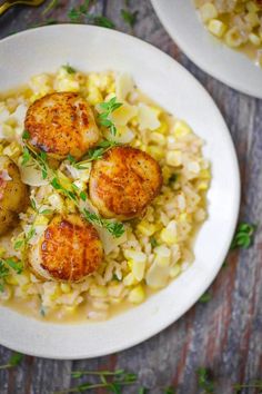 two white plates filled with rice and scallops on top of a wooden table