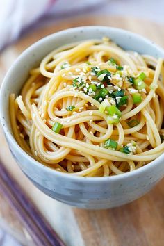 a bowl filled with noodles and topped with sesame seeds, scallions and green onions