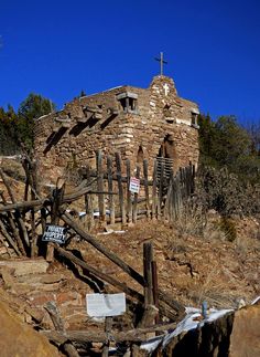 an old stone building on the side of a hill with a wooden fence around it