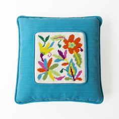 a blue pillow with colorful embroidered flowers on the front and sides, sitting on a white surface