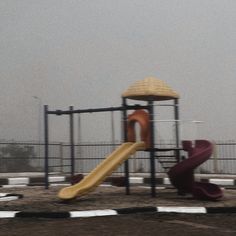 a children's play area with a slide and playground equipment in the background on a foggy day