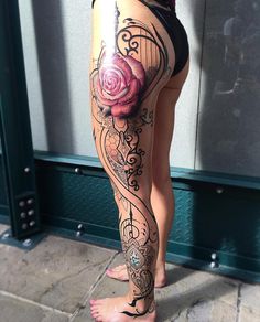 a woman's leg with tattoos and a rose on it, in front of a building