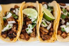 three tacos on a plate with lime wedges