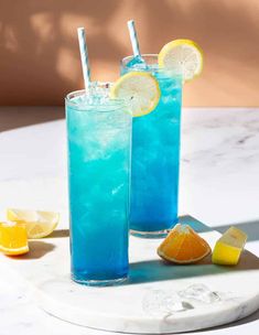 two glasses filled with blue liquid and lemon slices on a marble tray next to each other