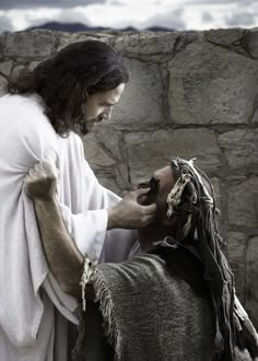 jesus with his hands on the head of a man in front of a stone wall