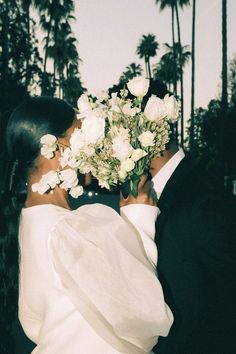 a bride and groom kissing each other in front of palm trees with white flowers on their forehead