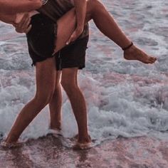 two people are standing in the water with their arms around each other and one is holding another person's leg