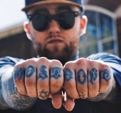 a man with tattoos on his fingers pointing at the camera while wearing a hat and sunglasses