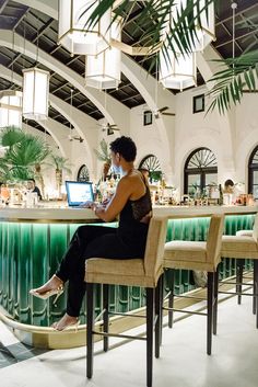 a woman sitting at a bar with a laptop on her lap and palm trees in the background