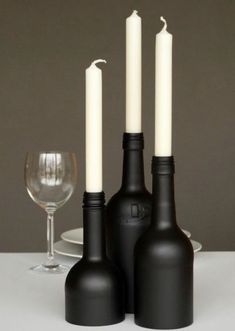 three wine bottles and two candles on a table