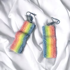 there are two rainbow colored earrings on the white bed sheet, one is made out of plastic