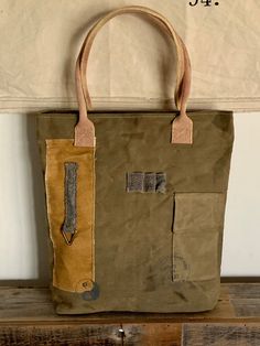 "Vintage military upcycled tent canvas tote handbag Colorations: Olive green, khaki gold, gray & cream Writing: Gray Vintage brass hardware Cream/wine double handles *Please note: All materials are upcycled. Colorations and fabric shading/distressing will vary. All fabric is best quality.  Specifications: 16x17x4\" 9\" double handle Top zippered closure Exterior back zippered pocket, front fold pocket  Interior 3 pockets (1 zippered) Key clip  Hand/paw ying/yang Unconstructed, but sturdy canvas" Khaki Canvas Tote Bag With Canvas Lining, Rectangular Khaki Canvas Bag With Handles, Khaki Canvas Tote Bag, Green Canvas Tote Bag For Outdoor Use, Green Tote Canvas Bag For Outdoor, Khaki Canvas Bag With Handles, Green Duck Canvas Tote Bag, Khaki Canvas Bag, Khaki Utility Canvas Bags