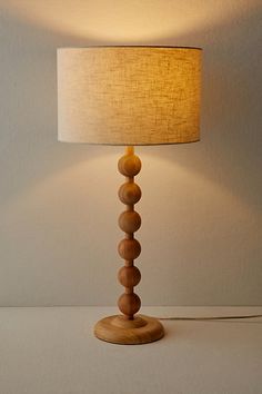 a wooden lamp on a table with a white shade over the top and a light that is turned on