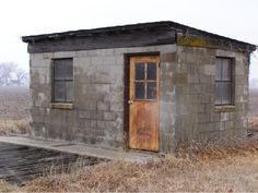 an old outhouse sits in the middle of a field with no grass on it