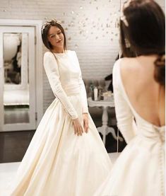 a woman in a white wedding dress looking at herself in the mirror with her back to the camera