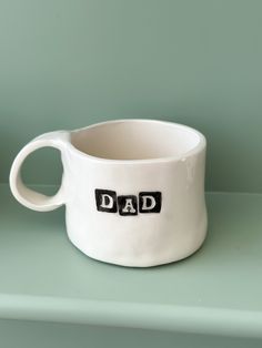 a white cup with the word dad written on it sitting on top of a shelf