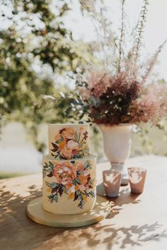 a wedding cake sitting on top of a wooden table next to a vase filled with flowers