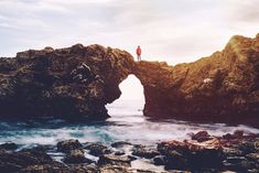 a man standing on top of a rock formation near the ocean with an oval logo over it