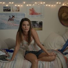 a woman sitting on top of a bed next to a wall with pictures and lights