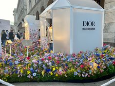 a flower bed with flowers in front of a dior store and people walking by