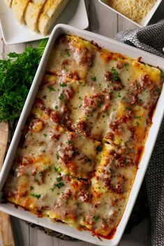 a casserole dish with meat and cheese in it on a wooden table next to bread